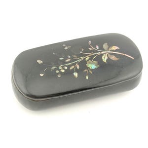 May include: A black, rectangular box with a hinged lid. The box is decorated with a floral design inlaid with iridescent mother-of-pearl. The box is likely used for storing small items, such as jewelry or trinkets.