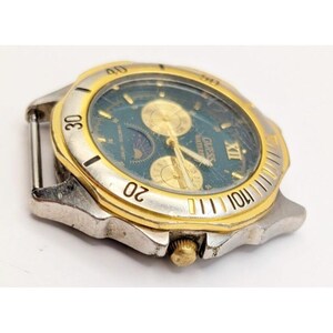 Op de afbeelding: Een zilveren en gouden Guess-horloge met een blauwe wijzerplaat en een maanfase-complicatie. Het horloge heeft een datumvenster en een chronograaf.