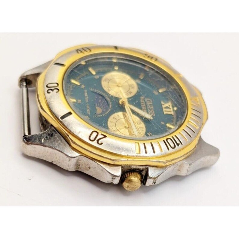 Op de afbeelding: Een zilveren en gouden Guess-horloge met een blauwe wijzerplaat en een maanfase-complicatie. Het horloge heeft een datumvenster en een chronograaf.