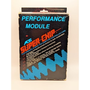 May include: A black box with the words "PERFORMANCE MODULE" in blue and "SUPER CHIP" in red and white. The box advertises performance improvements for computer-controlled cars, including optimized timing and fuel mixture. The box also mentions easy installation and a 5-year warranty.
