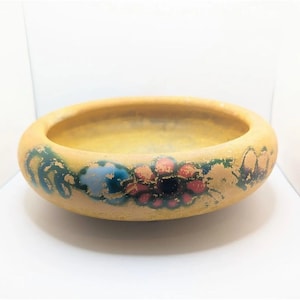 May include: A yellow ceramic bowl with a floral design. The bowl has a wide rim and a rounded bottom. The flowers are painted in shades of red, blue, and green.
