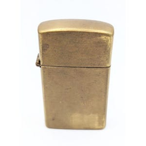 May include: A brass lighter with a worn finish. The lighter is closed and has a hinge on the side.