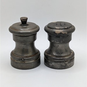 May include: A set of two vintage pewter salt and pepper shakers. The shakers are silver in color and have a classic design.