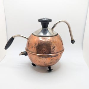 May include: A copper electric kettle with a black handle and a silver spout. The kettle has a round body and a black knob on top.