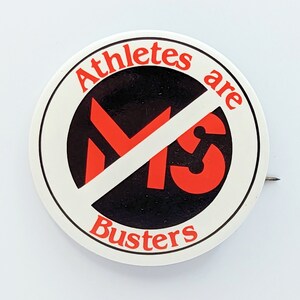 May include: A white button with a red slash through the letters "MS" and the text "Athletes are Busters" around the outside.
