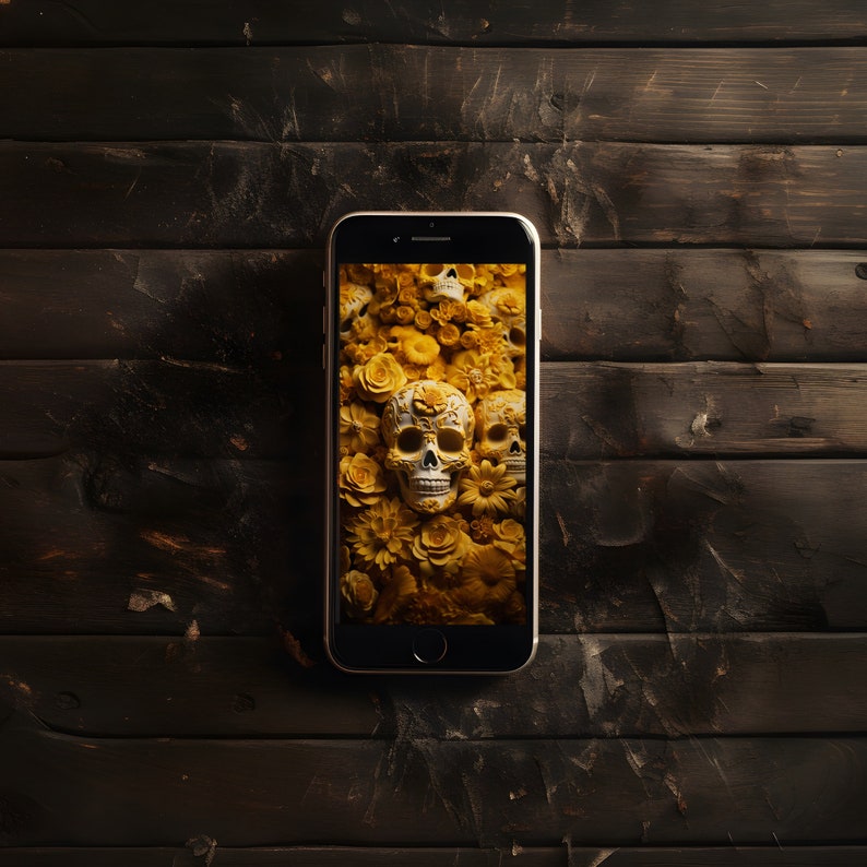 May include: A smartphone displaying a wallpaper of sugar skulls and yellow flowers. The phone is on a dark wood surface.
