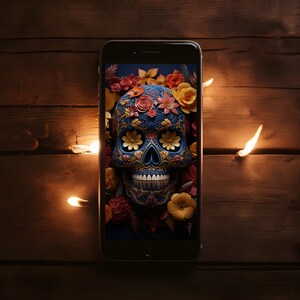 May include: A smartphone displaying a colorful sugar skull with floral decorations on a dark background. The skull is blue with gold accents and has a white smile. The flowers are yellow, orange, red, and pink.