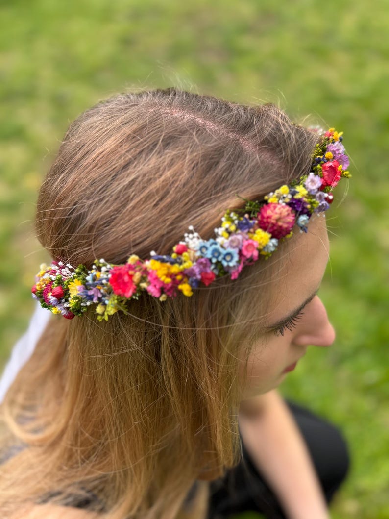 May include: A floral crown made of small, colorful flowers. The crown is worn on a person's head, with their brown hair visible.