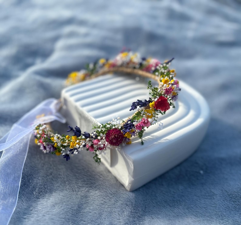 May include: A flower crown made with dried flowers in shades of pink, yellow, purple, and red. The crown is on a white surface.