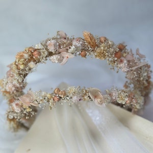 Pode incluir: Uma coroa de flores secas delicada com forma circular. A coroa &eacute; feita de pequenas flores brancas e bege, com algumas flores maiores de cor p&ecirc;ssego espalhadas. A coroa &eacute; perfeita para um casamento ou outra ocasi&atilde;o especial.
