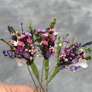 May include: Four gold hair clips with dried flower bouquets. Each bouquet features pink, purple, and white flowers with green foliage.