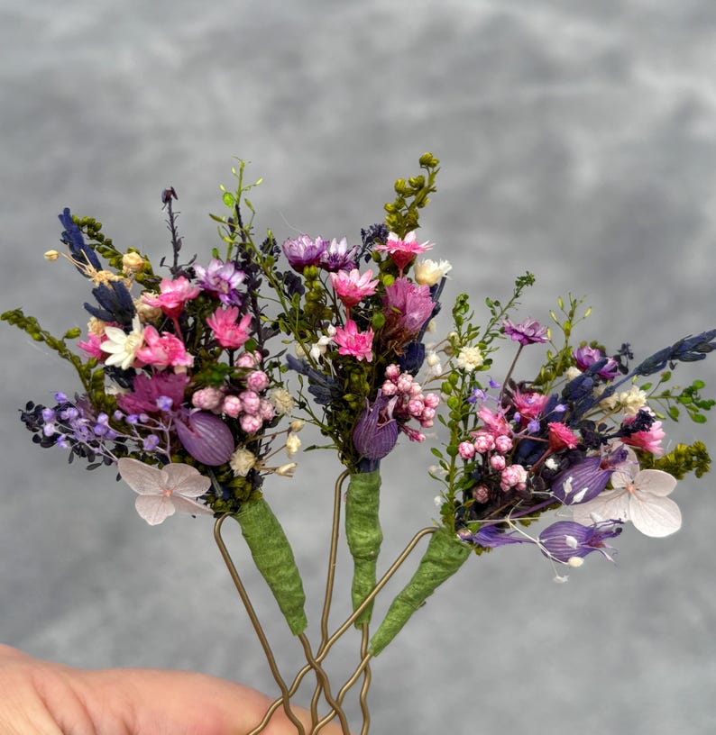 May include: Four gold hair clips with dried flower bouquets. Each bouquet features pink, purple, and white flowers with green foliage.