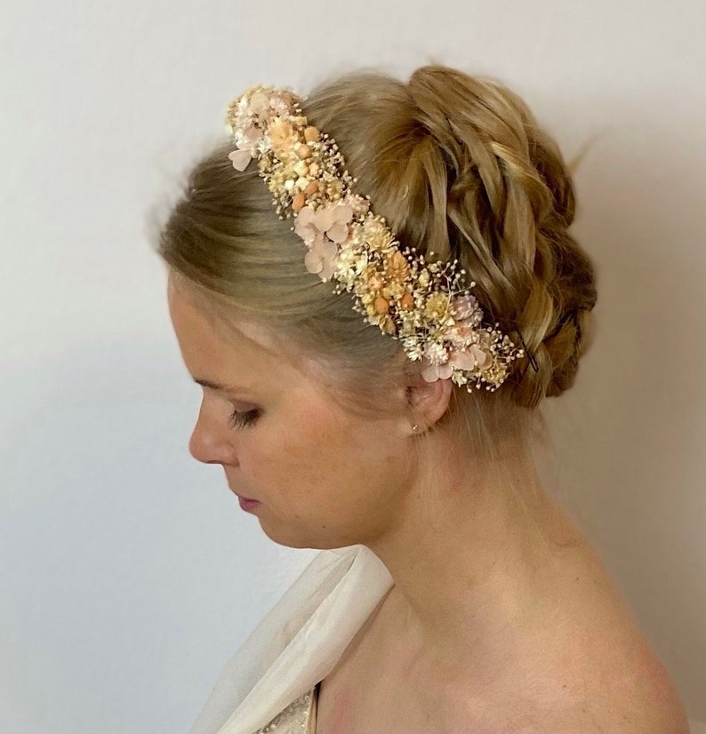 Pode incluir: Uma coroa de flores feita de flores secas em tons de p&ecirc;ssego, creme e bege. A coroa &eacute; usada por uma pessoa com cabelo loiro.