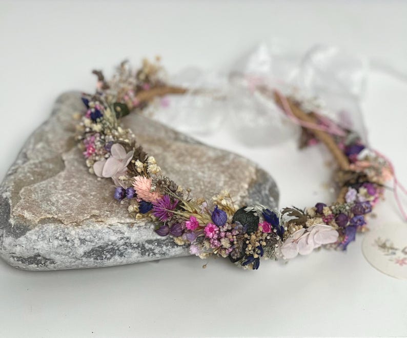 May include: A delicate floral crown made with dried flowers in shades of pink, purple, and white. The crown is made on a wire base and is perfect for a wedding or special occasion.