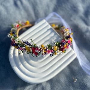 May include: A flower crown made of dried flowers in shades of pink, yellow, white, and purple. The crown is on a white surface.