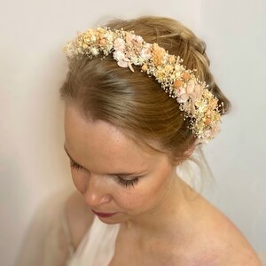 Pode incluir: Uma delicada coroa de flores secas em forma de faixa de cabe&ccedil;a, com flores em tons de creme, bege e rosa. A faixa de cabe&ccedil;a &eacute; usada por uma pessoa com cabelo loiro.