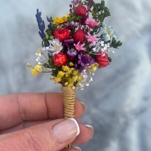 May include: A small bouquet of dried flowers in shades of red, yellow, purple, and blue, tied together with twine.