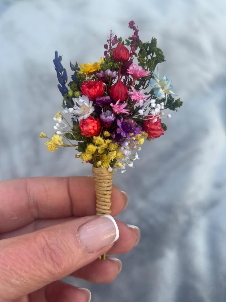 May include: A small bouquet of dried flowers in shades of red, yellow, purple, and blue, tied together with twine.