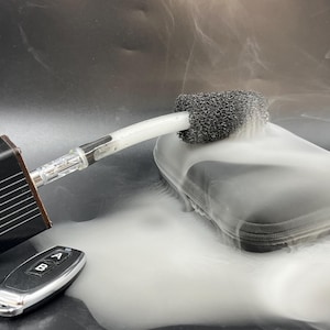 Könnte beinhalten: Eine schwarze Box mit einem weißen Schlauch, der an einem schwarzen Schwamm befestigt ist. Der Schlauch ist mit einer Fernbedienung mit zwei Knöpfen mit der Aufschrift A und B verbunden. Die Box und der Schwamm sind von weißem Rauch umgeben.