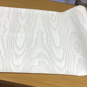 May include: A roll of white woodgrain contact paper. The paper has a subtle embossed texture.