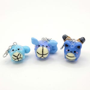 May include: Three blue and white ceramic keyrings shaped like cartoon characters. Each keyring features a different character design with a basketball.