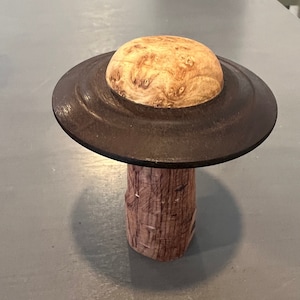 May include: A wooden mushroom-shaped sculpture with a brown top and a light brown stem. The top of the sculpture is made of wood with a burl pattern.