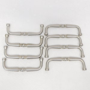 Könnte beinhalten: Acht silberne Schrankgriffe mit einem dekorativen Design. Die Griffe sind in einer Reihe angeordnet, wobei der obere Griff oben im Bild und der untere Griff unten im Bild ist.