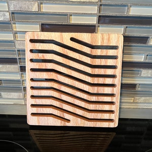 May include: A wooden kitchen counter top with a brown and beige tiled backsplash. A wooden trivet with a geometric pattern is sitting on the counter top.