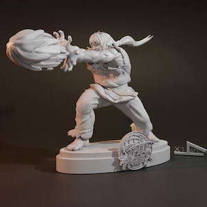 Könnte beinhalten: Eine graue 3D-gedruckte Figur eines Charakters aus Street Fighter, mit einer feurigen Faust ausgestreckt. Die Figur ist in einer Kampfhaltung posiert und steht auf einem Sockel mit dem Street Fighter-Logo.
