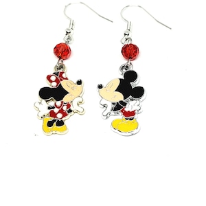 May include: Dangle earrings featuring Mickey and Minnie Mouse. The earrings have a red bead at the top, with the characters in black, white, red, and yellow. Minnie has a red bow with white polka dots.
