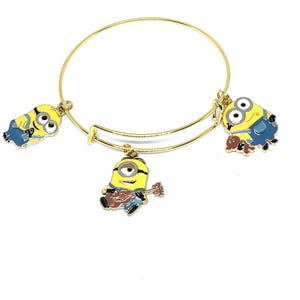Puede incluir: Pulsera de brazalete ajustable dorada con tres colgantes de Minions coloridos. Los colgantes representan a los Minions en varias poses, incluido uno tocando el ukelele. La pulsera es un accesorio divertido para los fans de la película animada.