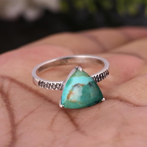 May include: A silver ring with a triangular turquoise gemstone. The ring has a textured band and a polished finish. The turquoise stone displays a mix of blue and brown colours.