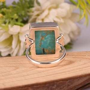 May include: A silver ring with a rectangular turquoise stone. The stone has a mottled blue-green color with brown veining. The ring has decorative side accents and a polished finish.