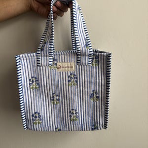 Handmade quilted cotton mini tote bag featuring blue vertical stripes with floral motifs, matching striped handles, and padded cotton construction.