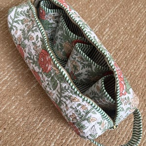 Floral hand block printed Dyson organizer bag opened to reveal four padded interior pockets, striped cotton lining, and spacious storage for Dyson Airwrap attachments.