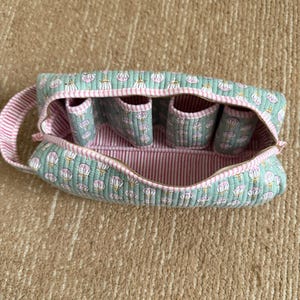 Handmade quilted cotton travel toiletry bag featuring a mint green floral block print, pink striped lining, four built-in brush slots, zipper closure, and sturdy carry handle.