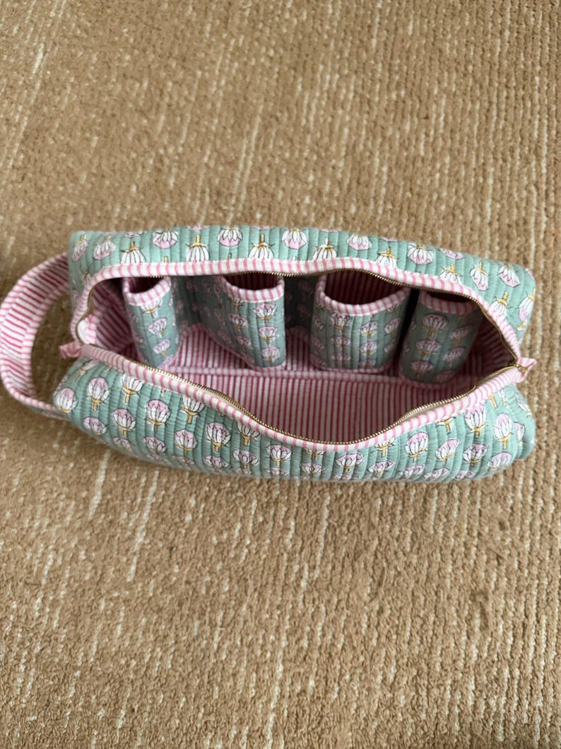 Handmade quilted cotton travel toiletry bag featuring a mint green floral block print, pink striped lining, four built-in brush slots, zipper closure, and sturdy carry handle.