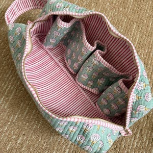 Open sage green quilted Dyson Airwrap storage case featuring four padded attachment pockets, spacious interior, striped cotton lining, and premium zipper closure.