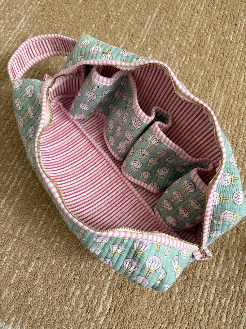 Open sage green quilted Dyson Airwrap storage case featuring four padded attachment pockets, spacious interior, striped cotton lining, and premium zipper closure.