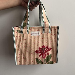 Handmade quilted cotton mini tote bag in soft beige with red lily flower print and green striped handles, ideal as a lunch bag or everyday carry tote.