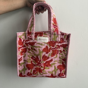 Handmade quilted cotton mini tote bag with pink floral block print, striped pink handles, and lightweight padded design for daily essentials.