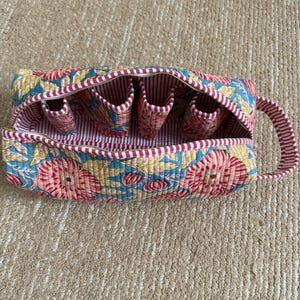 Quilted cotton blue floral hair tool organizer with red striped trim and carry handle.