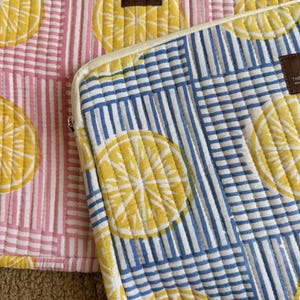 May include: Two quilted fabric cases with lemon slice patterns. One case has a pink and white striped background, while the other has a blue and white striped background. Both cases feature yellow lemon slice designs.