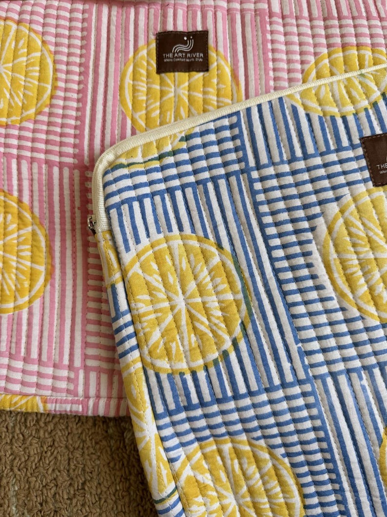 May include: Two quilted fabric cases with lemon slice patterns. One case has a pink and white striped background, while the other has a blue and white striped background. Both cases feature yellow lemon slice designs.
