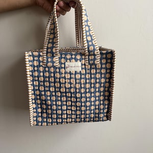 Handmade quilted cotton mini tote bag in indigo blue with beige polka dot print, striped mustard handles, and structured design for carrying daily essentials.