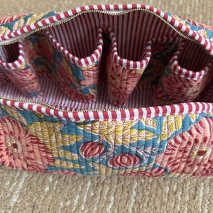Open floral quilted Dyson storage case with four interior pockets, red striped cotton lining, premium YKK zipper, and organized compartments for Dyson attachments.