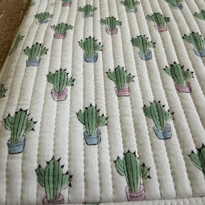 May include: White quilted laptop sleeve featuring a repeating pattern of green cacti in blue and pink pots. The sleeve has a zip closure and a label that reads "The Art River".