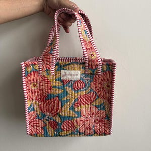 Handmade quilted cotton mini tote bag with coral pink floral print on a blue background, striped handles, and padded structure for everyday use.