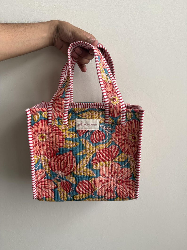 Handmade quilted cotton mini tote bag with coral pink floral print on a blue background, striped handles, and padded structure for everyday use.