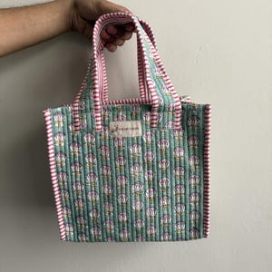Handmade quilted cotton mini tote bag in mint green with lotus flower print, striped pink handles, and soft quilted structure for stylish everyday use.